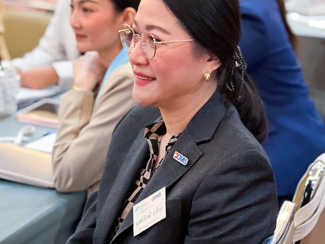 ผู้เข้าร่วมยิ้มขณะนั่งฟังที่โต๊ะ